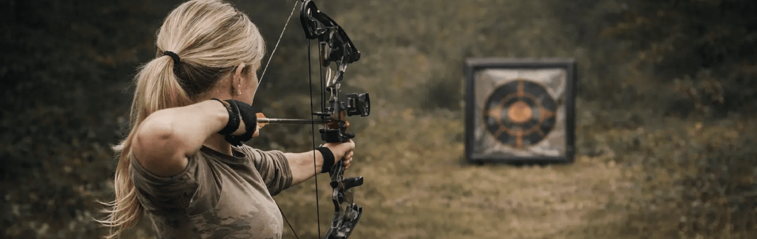 Kvinde træner skydeteknik med compoundbue mod mål i skoven